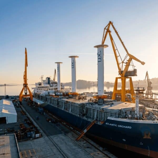 Puente grúa en puerto con barco y grúas de carga en el fondo.