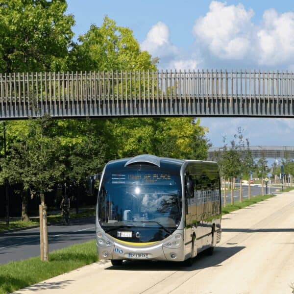 Autobús eléctrico moderno en la ciudad con puente peatonal y árboles verdes.